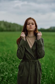 a beautiful woman stands in a green field and adjusts her coat. High quality photo