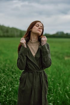 a beautiful woman stands in a green field and adjusts her coat. High quality photo