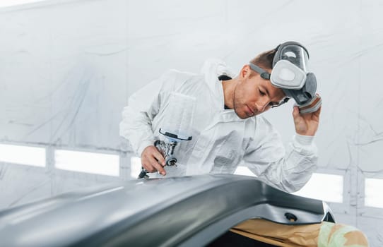 Painting the car. Man in uniform is working in the auto service.