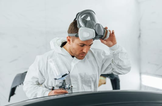 Painting the car. Man in uniform is working in the auto service.