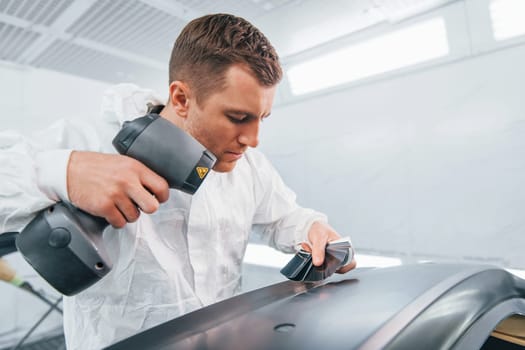 Working with car surface. Man in uniform is working in the auto service.