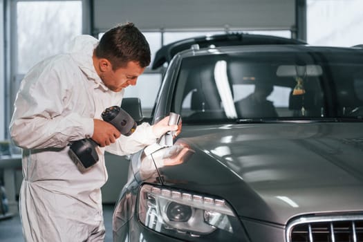 Using special equipment. Man in uniform is working in the auto service.