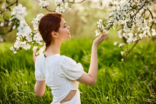 Young attractive woman with straight long hair standing in flowering Apple orchards. Beauty smiling woman looking at white flower. High quality photo