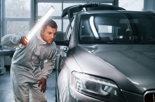 Silver colored car. Man in uniform is working in the auto service.