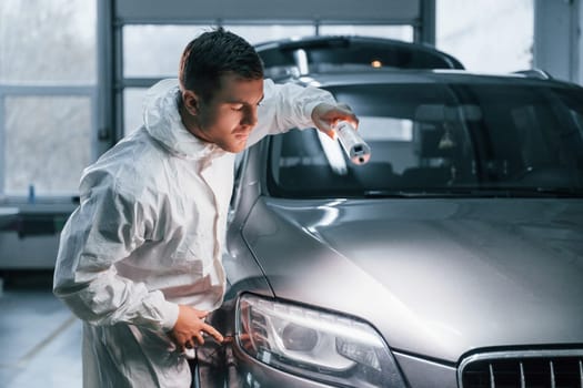 Silver colored car. Man in uniform is working in the auto service.