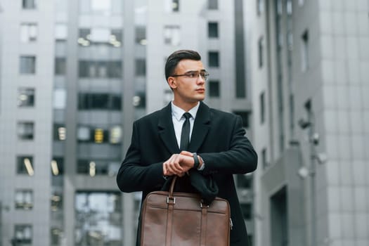 Checking the time. Businessman in black suit and tie is outdoors in the city.