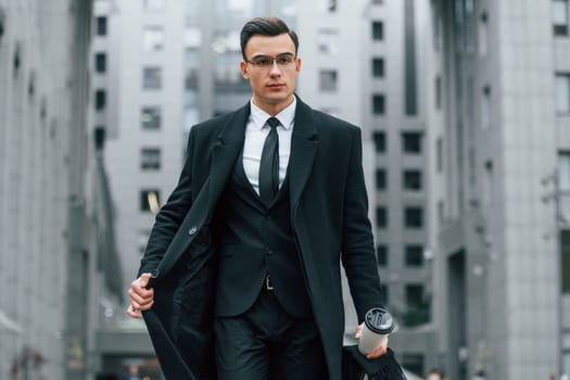 Walking forward. Businessman in black suit and tie is outdoors in the city.