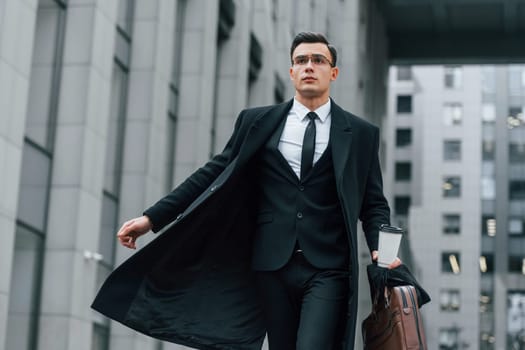 Walking forward. Businessman in black suit and tie is outdoors in the city.