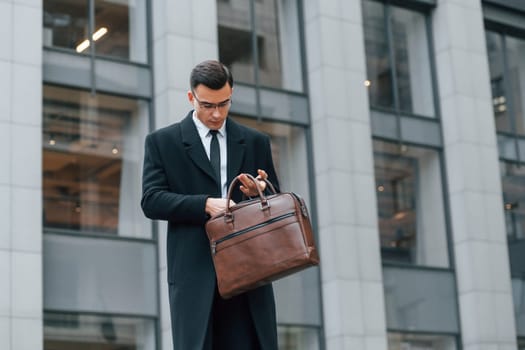 With brown bag. Businessman in black suit and tie is outdoors in the city.