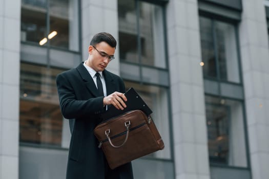 With brown bag. Businessman in black suit and tie is outdoors in the city.