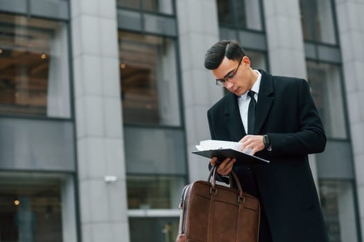 With brown bag. Businessman in black suit and tie is outdoors in the city.