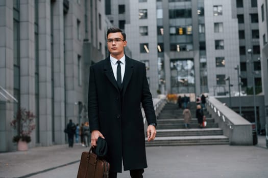 Front view. Businessman in black suit and tie is outdoors in the city.