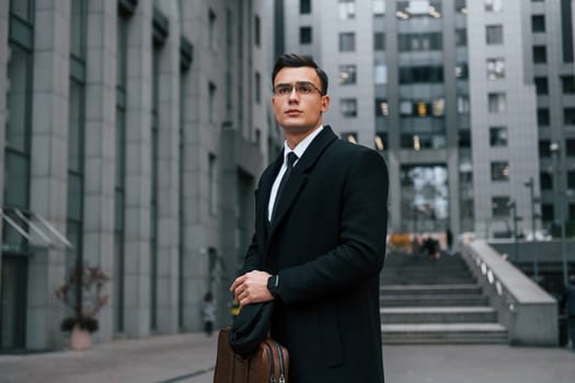 Front view. Businessman in black suit and tie is outdoors in the city.