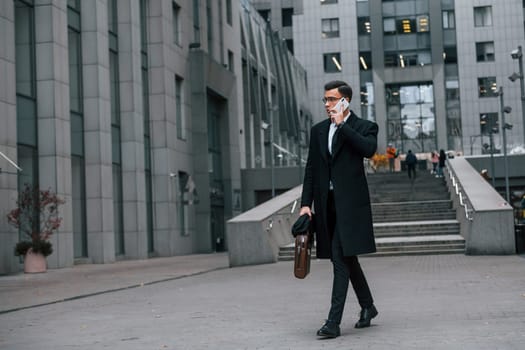 Phone in hand. Businessman in black suit and tie is outdoors in the city.