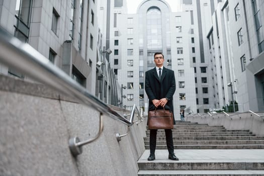 Buildings exterior. Businessman in black suit and tie is outdoors in the city.