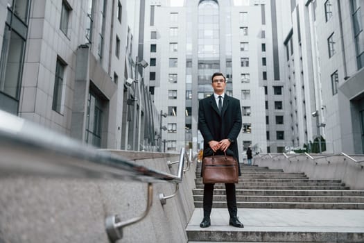 Buildings exterior. Businessman in black suit and tie is outdoors in the city.