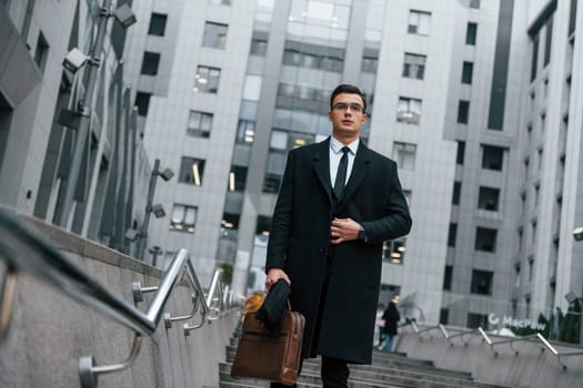 Buildings exterior. Businessman in black suit and tie is outdoors in the city.