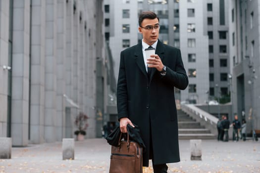 Buildings exterior. Businessman in black suit and tie is outdoors in the city.