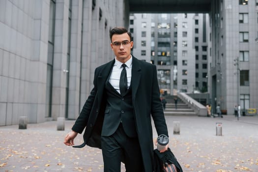 Walking forward. Businessman in black suit and tie is outdoors in the city.