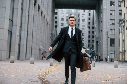 Going to work. Businessman in black suit and tie is outdoors in the city.