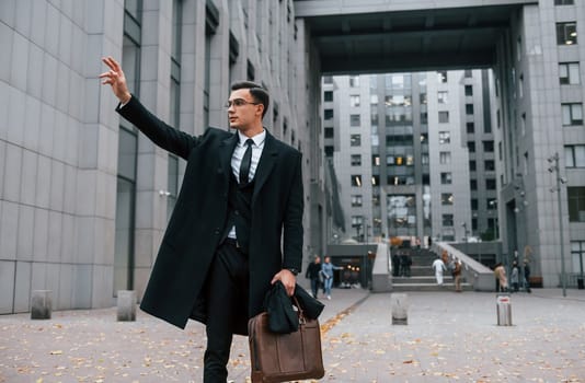 Looking for a taxi. Businessman in black suit and tie is outdoors in the city.