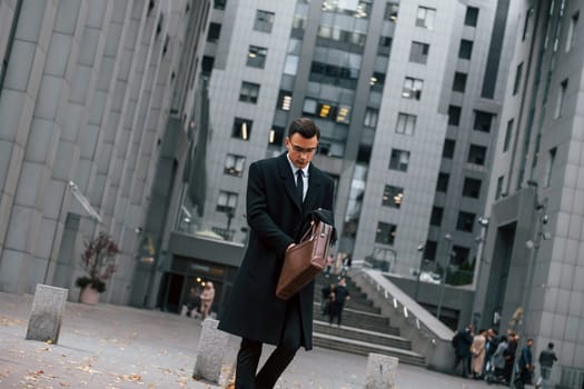 In formal clothes. Businessman in black suit and tie is outdoors in the city.