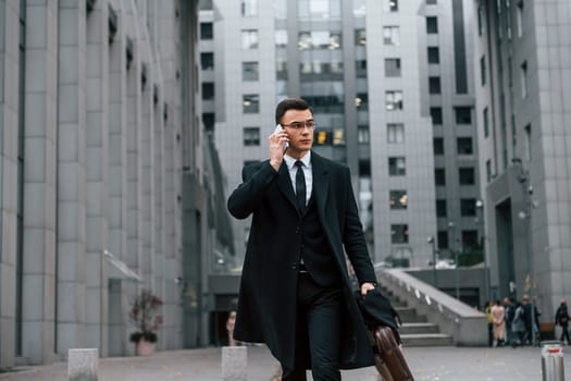 In formal clothes. Businessman in black suit and tie is outdoors in the city.
