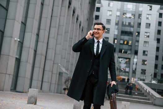 In formal clothes. Businessman in black suit and tie is outdoors in the city.