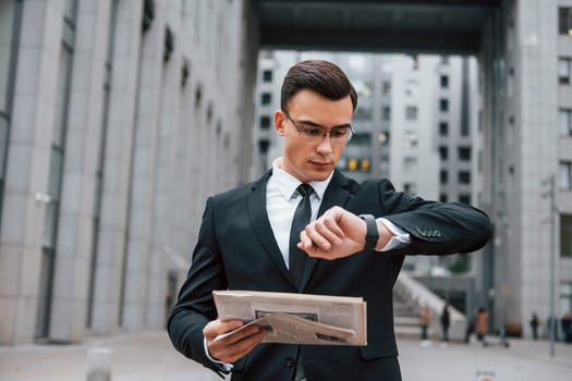 Checking the time. Businessman in black suit and tie is outdoors in the city.