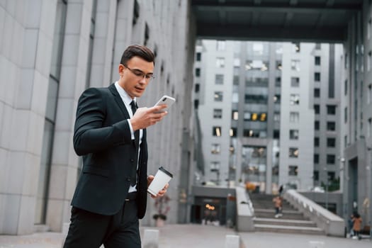 Internet communication by using smartphone. Businessman in black suit and tie is outdoors in the city.