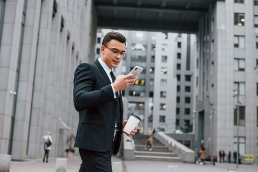 Internet communication by using smartphone. Businessman in black suit and tie is outdoors in the city.