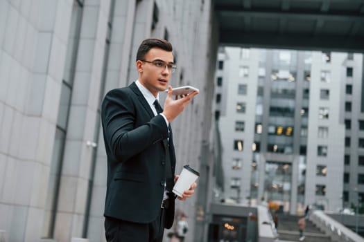 Internet communication by using smartphone. Businessman in black suit and tie is outdoors in the city.
