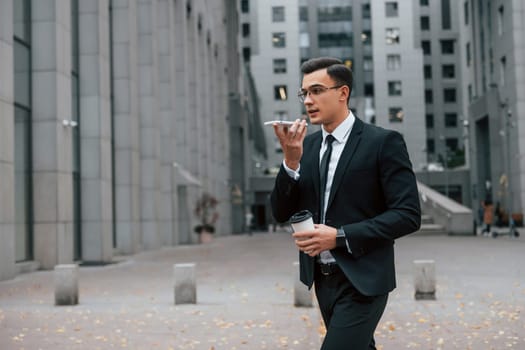Internet communication by using smartphone. Businessman in black suit and tie is outdoors in the city.