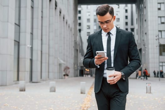 Internet communication by using smartphone. Businessman in black suit and tie is outdoors in the city.