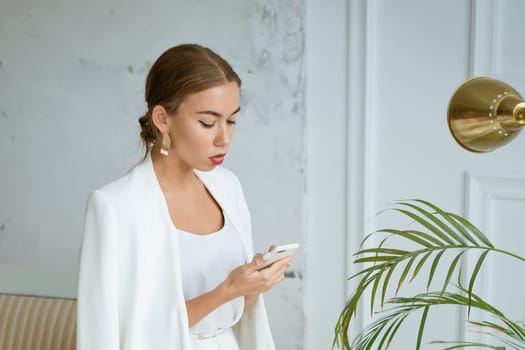 Successful young and beautiful woman of Caucasian ethnicity in a white jacket and dress talking on the phone, beautiful make-up hairstyle. Happy confident girl