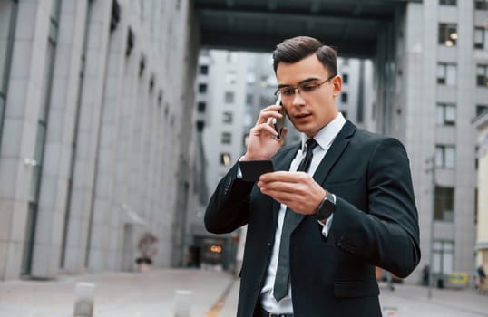 Busy man. Businessman in black suit and tie is outdoors in the city.