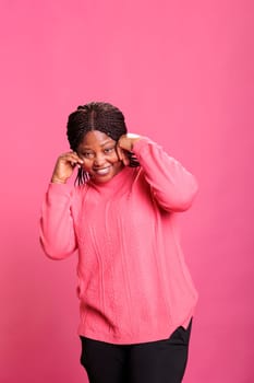 Young cheerful adult fooling around and being silly in studio, having fun in front of camera over background. Casual excited woman being positive and optimistic, enjoying laugh and smiling.
