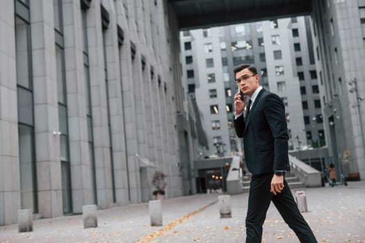 Busy man. Businessman in black suit and tie is outdoors in the city.