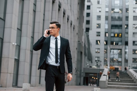 Busy man. Businessman in black suit and tie is outdoors in the city.