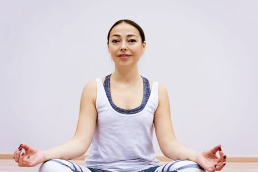 Happy caucasian woman in sportswear practices yoga at home against a wall background. The concept of a healthy lifestyle and inner spirit. Body concentration