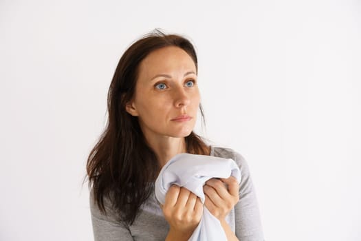 A cute Caucasian woman holding a clean white scent shirt on a light background. The concept of home care for clothing