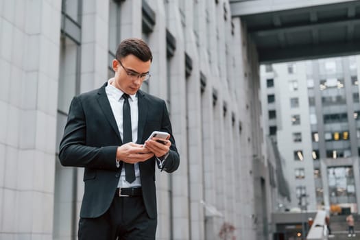 Busy man. Businessman in black suit and tie is outdoors in the city.