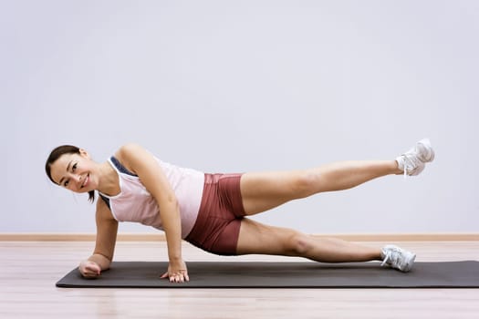 Happy caucasian woman in sportswear practices yoga at home against a wall background. The concept of a healthy lifestyle and inner spirit. Body concentration