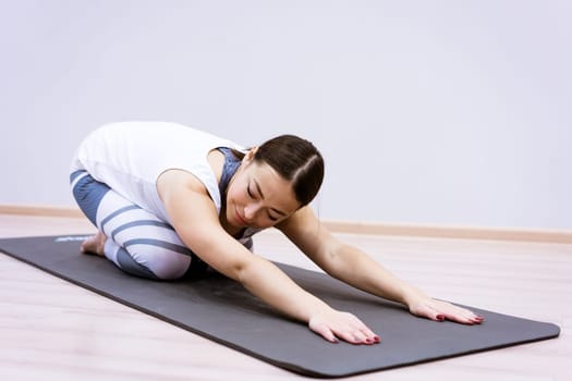 Happy caucasian woman in sportswear practices yoga at home against a wall background. The concept of a healthy lifestyle and inner spirit. Body concentration