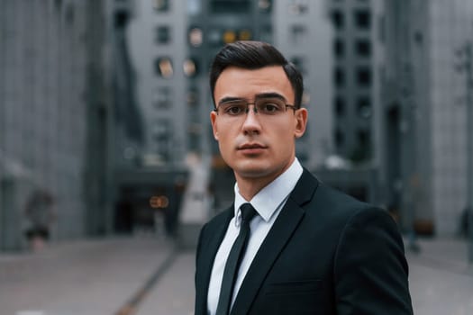 Portrait of businessman that is in black suit and tie is outdoors in the city.