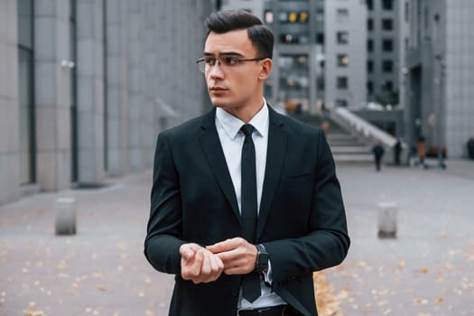 Portrait of businessman that is in black suit and tie is outdoors in the city.