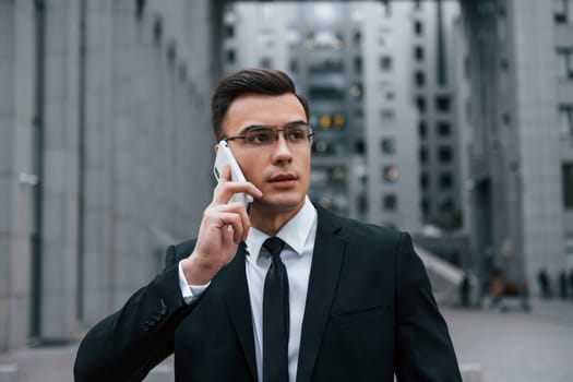 Portrait of businessman that is in black suit and tie is outdoors in the city.