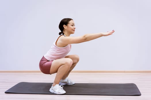 A woman of Caucasian ethnicity in sportswear is engaged in fitness at home against the background of a wall. Healthy lifestyle and slim body concept
