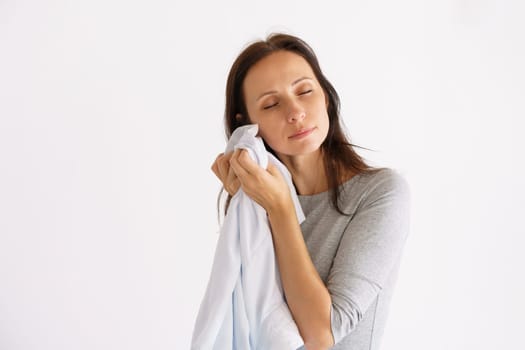 A cute Caucasian woman holding a clean white scent shirt on a light background. The concept of home care for clothing