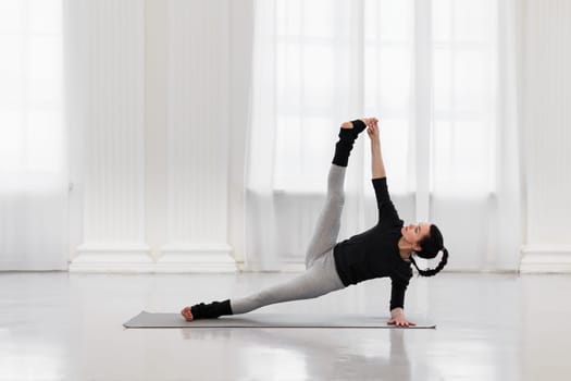 Charming young woman doing vertical splits during yoga class in a cozy gym. The concept of flexibility, leg and back muscle tone, balance and concentration.